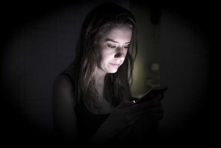 Woman looking at phone blue light at night, not able to sleep.