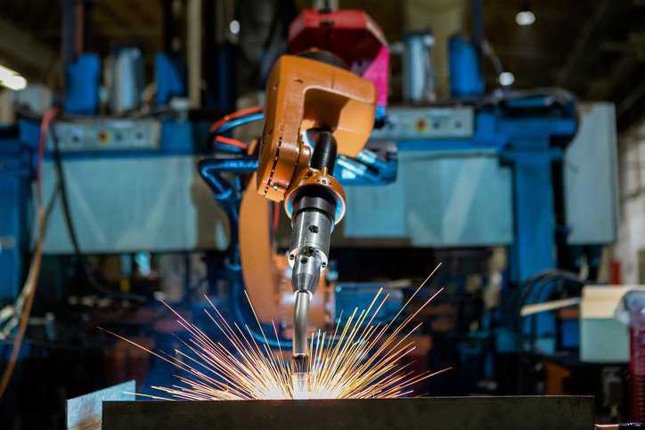 Robot is welding assembly automotive part in car factory, while adhering to AWS D16.1M/D16.a:2018 robotic arc welding requirements.