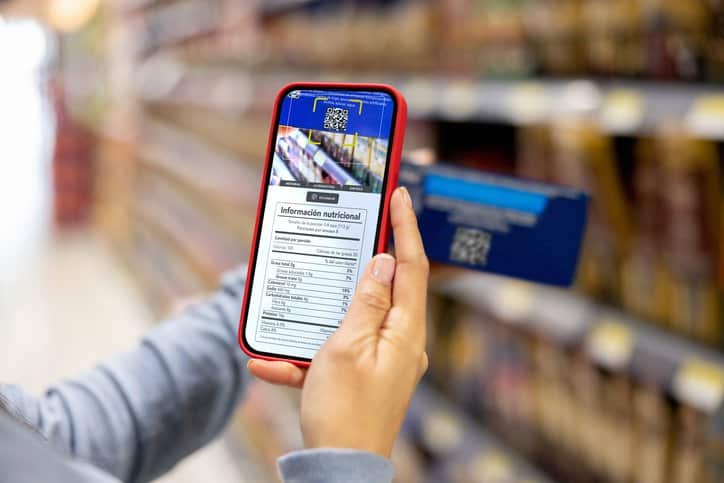 Close-up on a woman shopping at the supermarket and scanning a product barcode label, which adheres to ISO/IEC 15415:2024, with her cell phone to view the nutritional information.