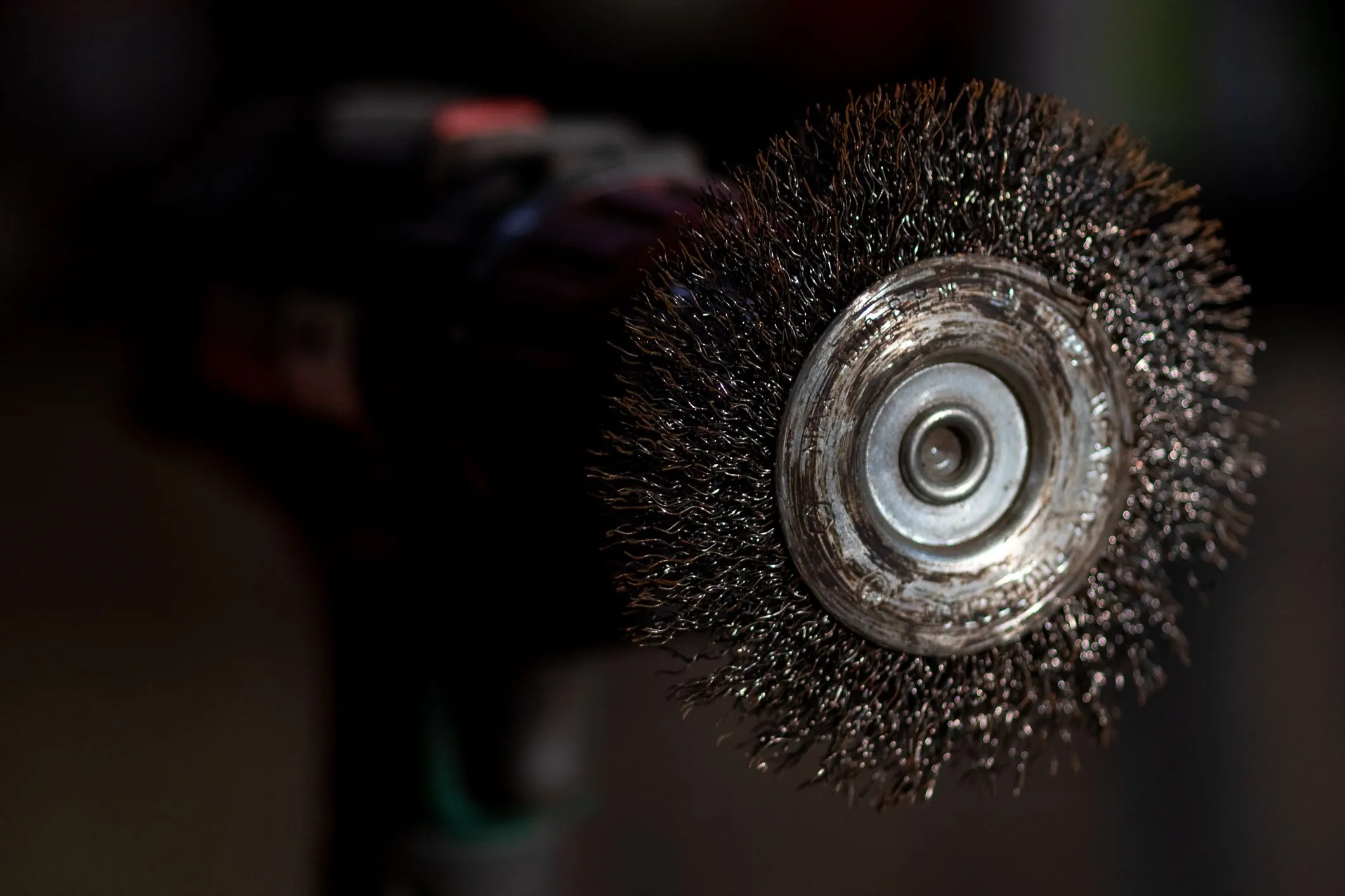Steel power-driven brush, adhering to ANSI B165.1-2026, that is cleaning off old metal sheet with rust.