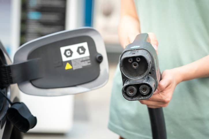 A man holding a DC charger socket head to charge his electric vehicle while adhering to IEEE Test Suite Specification: Electric Vehicles.