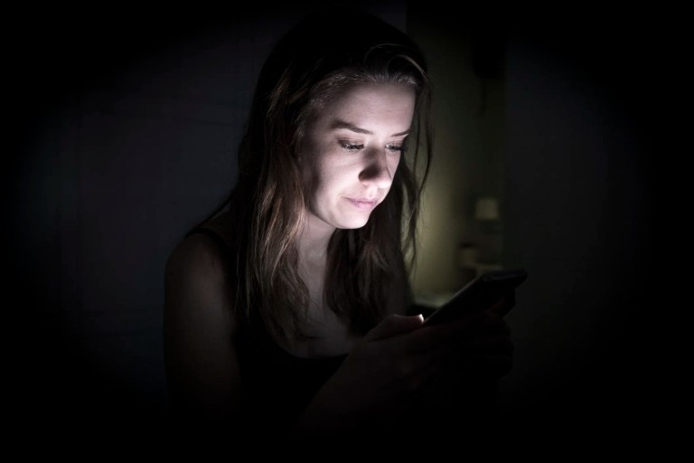 Woman looking at phone blue light at night, not able to sleep.