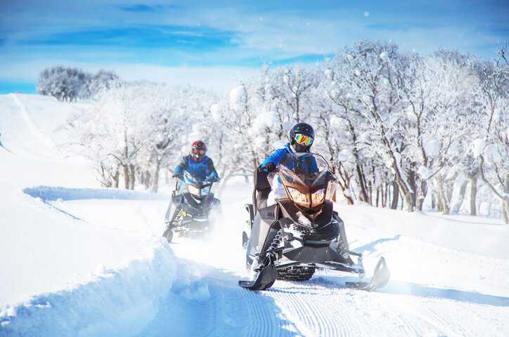 Two friends on a perfect snowy winter day heading down the snowy slopes on snowmobiles that adhere SAE J 292-2021.