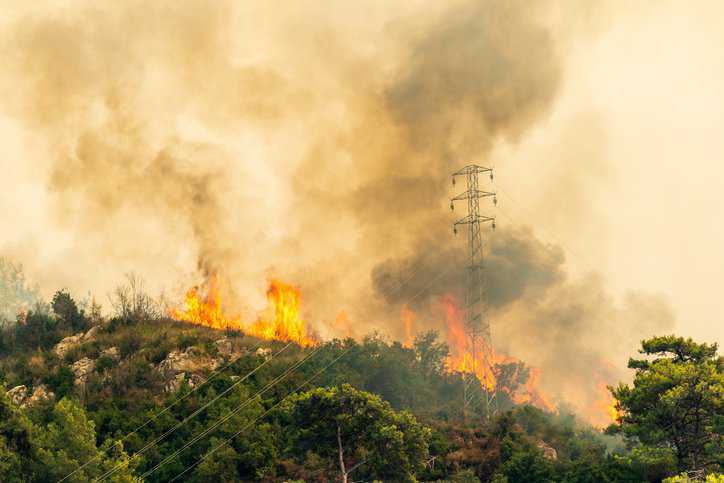 Wildfire causing damage to a transmission and distribution line structure, requiring fire safety guidance from AMPP TR1505-2022.