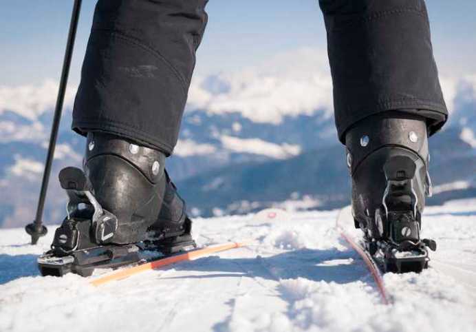 Skier with black boots at top of slope and ready for expert trail with higher DIN setting.