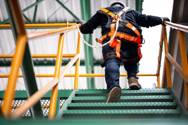 Worker walking up stairs wearing orange safety harness after being cited by OSHA for violating fall protection rules.