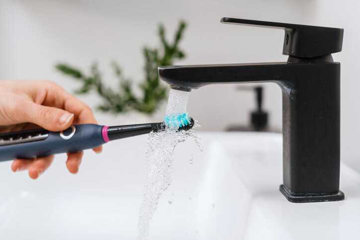 A consumer using an electric toothbrush, which adheres to ISO 20127:2020, to brush her teeth.
