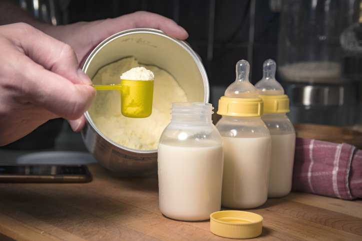 Mother measuring the amount of infant formula, which adheres to ISO 20636:2018, to give to her baby.