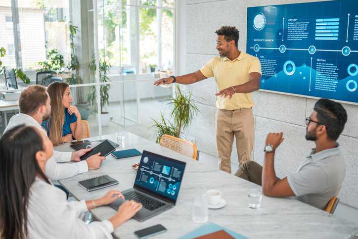 Marketing professionals collaborate using laptops and wireless technology, contributing to a dynamic exchange of ideas to promote sales, while adhering to ISO 20252 market research guidelines.