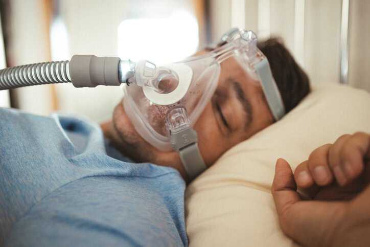 Middle aged man sleeping with CPAP machine mask on for sleep apnea that adheres to ISO 80601-2-70 and ISO 17510.