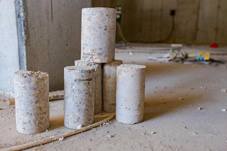 A few concrete cylindrical pillars placed on the floor of building under construction drilled for quality testing to assure compliance to ASTM C31/C31M-25a.