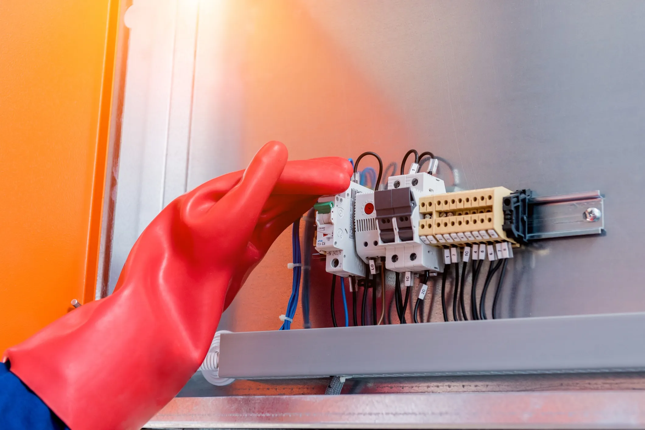 An engineer wearing rubber gloves that adhere to ASTM F1236-25 fixes electrical equipment.