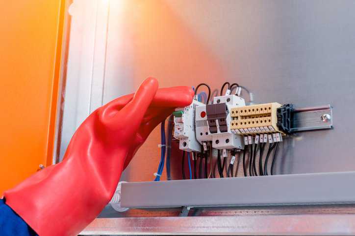 An engineer wearing rubber gloves that adhere to ASTM F1236-25 fixes electrical equipment.