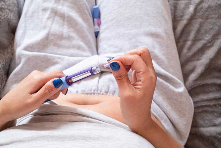 An overweight woman sitting on the couch with Type-2 Diabetes holding a syringe containing the GLP-1 drug, Ozempic.