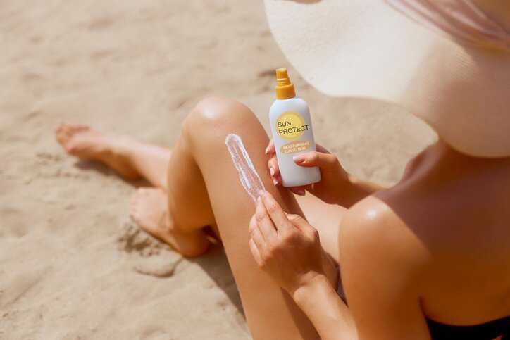 Woman applying sunscreen at the beach that complied with ISO 2444:2019 in vivo determination of SPF requirements.