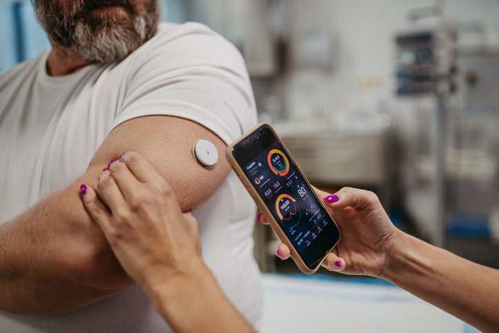 Doctor connecting patient's continuous glucose monitor with a connected diabetes devices, which adheres to IEEE 2621.1-2022, to check his blood sugar level in real time.