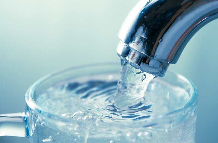 Close-up view of water flowing from tap into glass that adhered to NSF P524-2023 requirements for water quality testing devices.