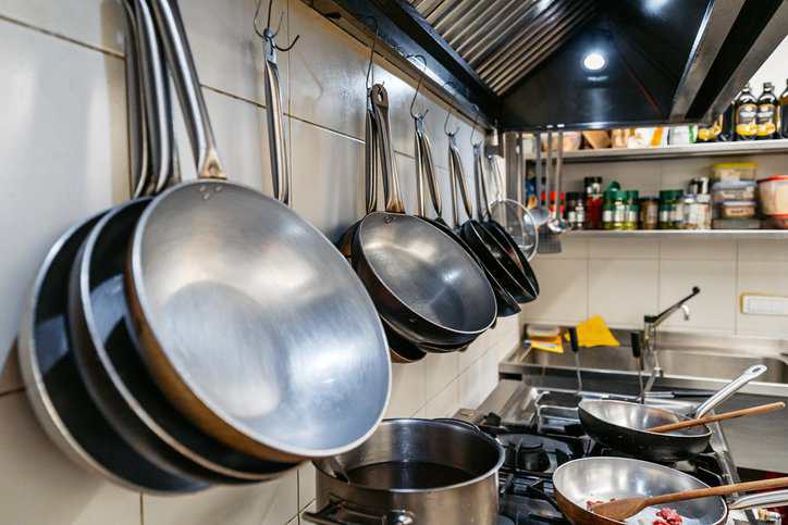 Pans and pots hanging on the wall in a commercial kitchen after getting cleaned and sanitized in a residential pots and pans washing machine that adheres to NSF P180.