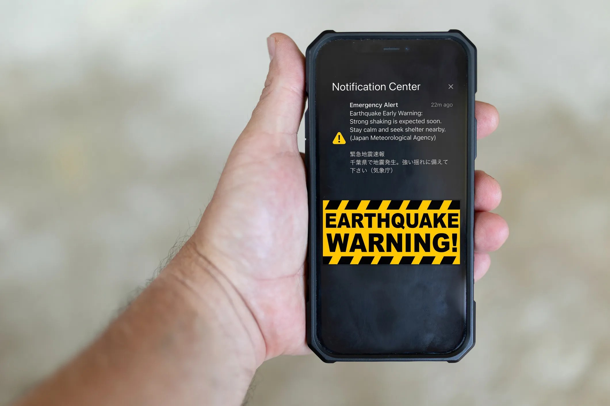 A smartphone with a hazard message in yellow and black about an earthquake that adheres to ANSI Z535.7-2024 guidelines for electronic media safety communications requirements.