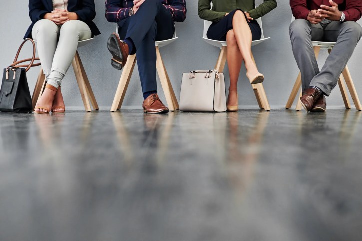 Line of business people's legs while they wait in chairs for interview.