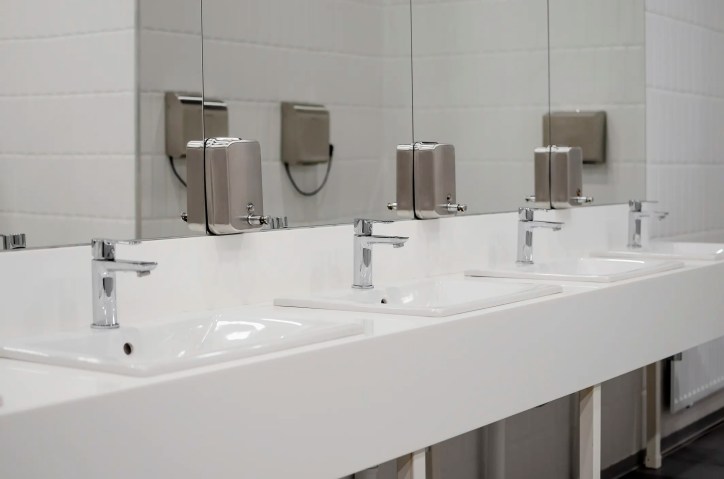 Restroom sinks lined up with chrome faucets.