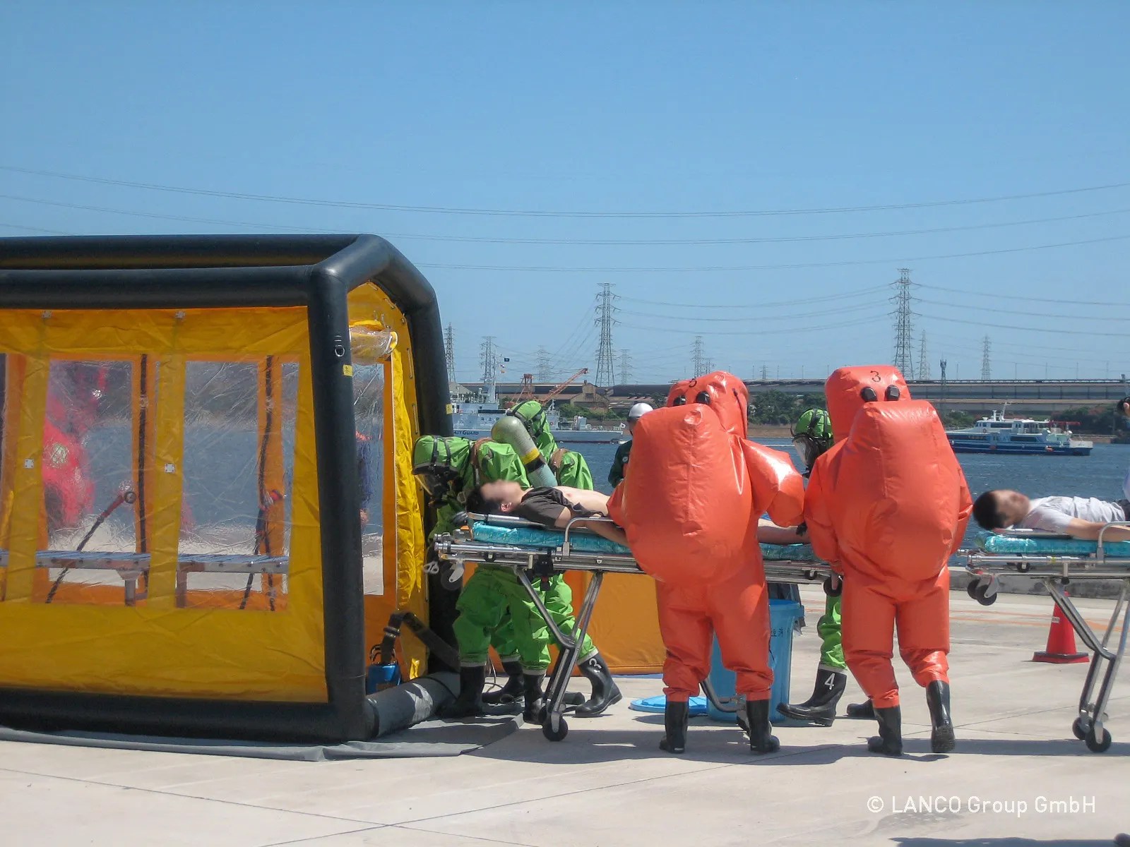 A group of people in orange suits standing around a decontamination shower tent.