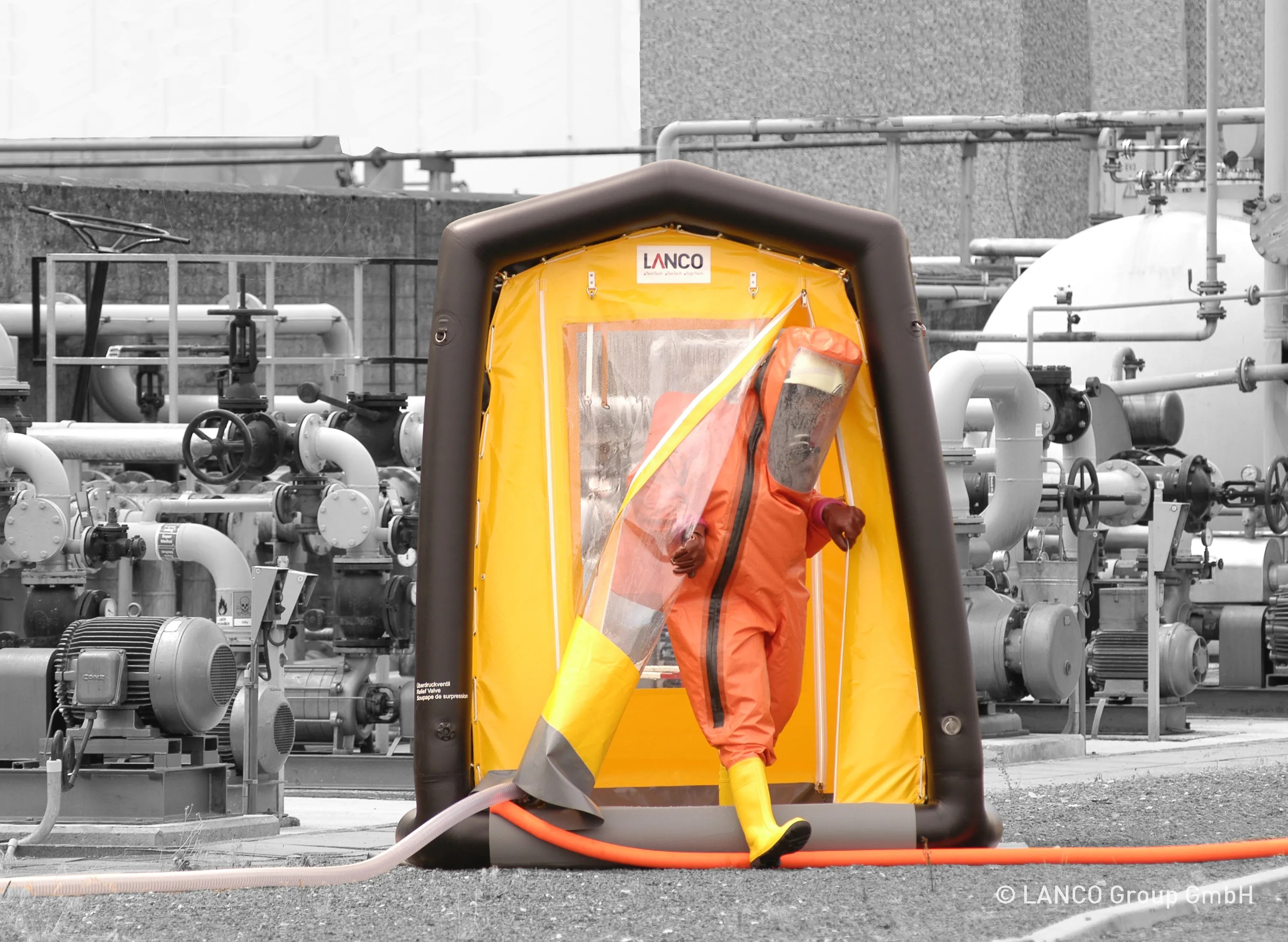 A man in an orange suit standing next to a decontamination shower.