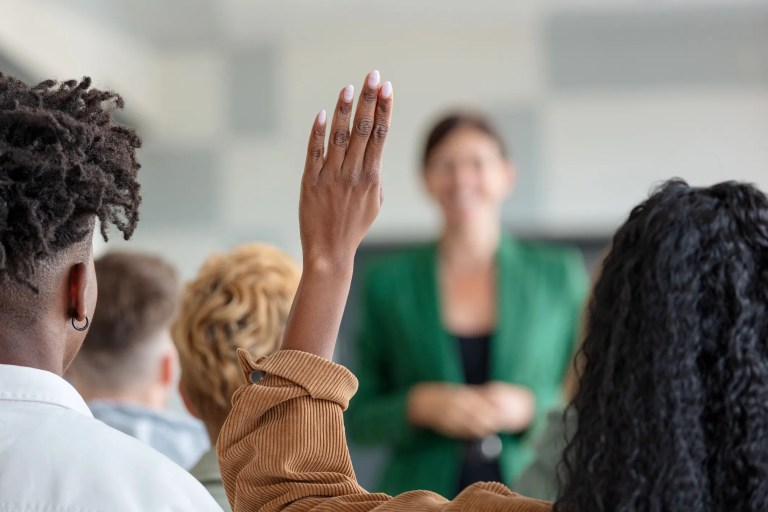 A group of people raising their hands in front of a teacher.