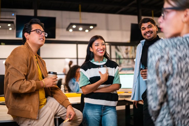 Employees in a modern office environment engaging in open conversation, symbolizing psychological safety and mental health support in the workplace that has implemented ISO 45003:2021 principles.