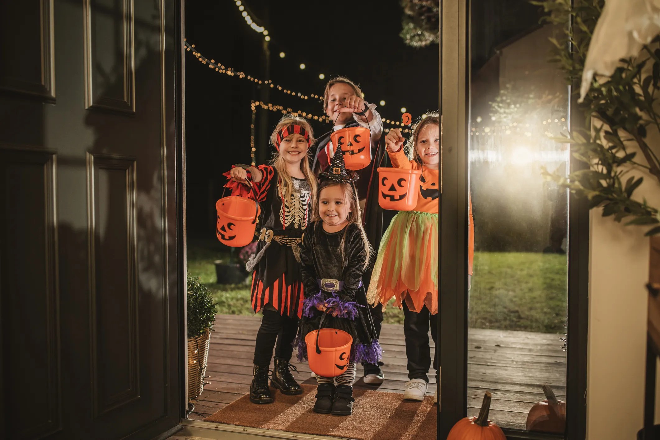 Children in Halloween costumes trick-or-treating at night, carrying toy props like plastic pumpkins and swords. Image highlights the importance of safety standards like ASTM F963-23 and ISO 8124-1:2022, which help ensure costumes and accessories are safe for children under 14 by addressing risks like flammability and choking hazards.