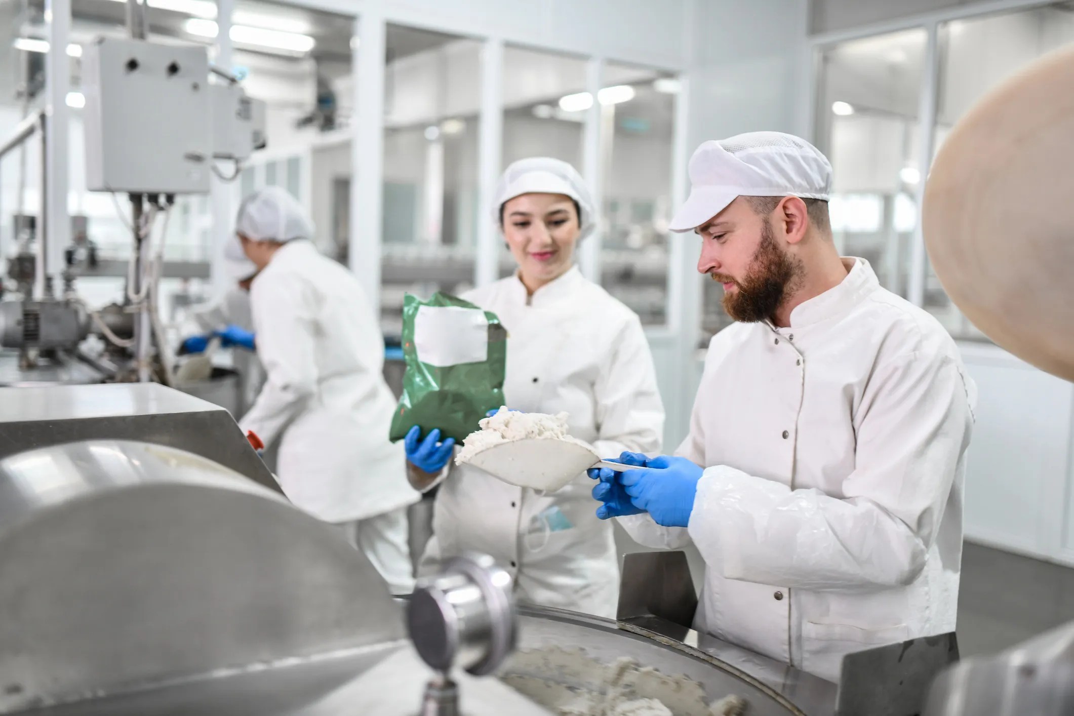 Workers in a food processing plant preparing cottage cheese according to ISO 23319:2022 and ISO 8262-3:2005 food safety testing methods.