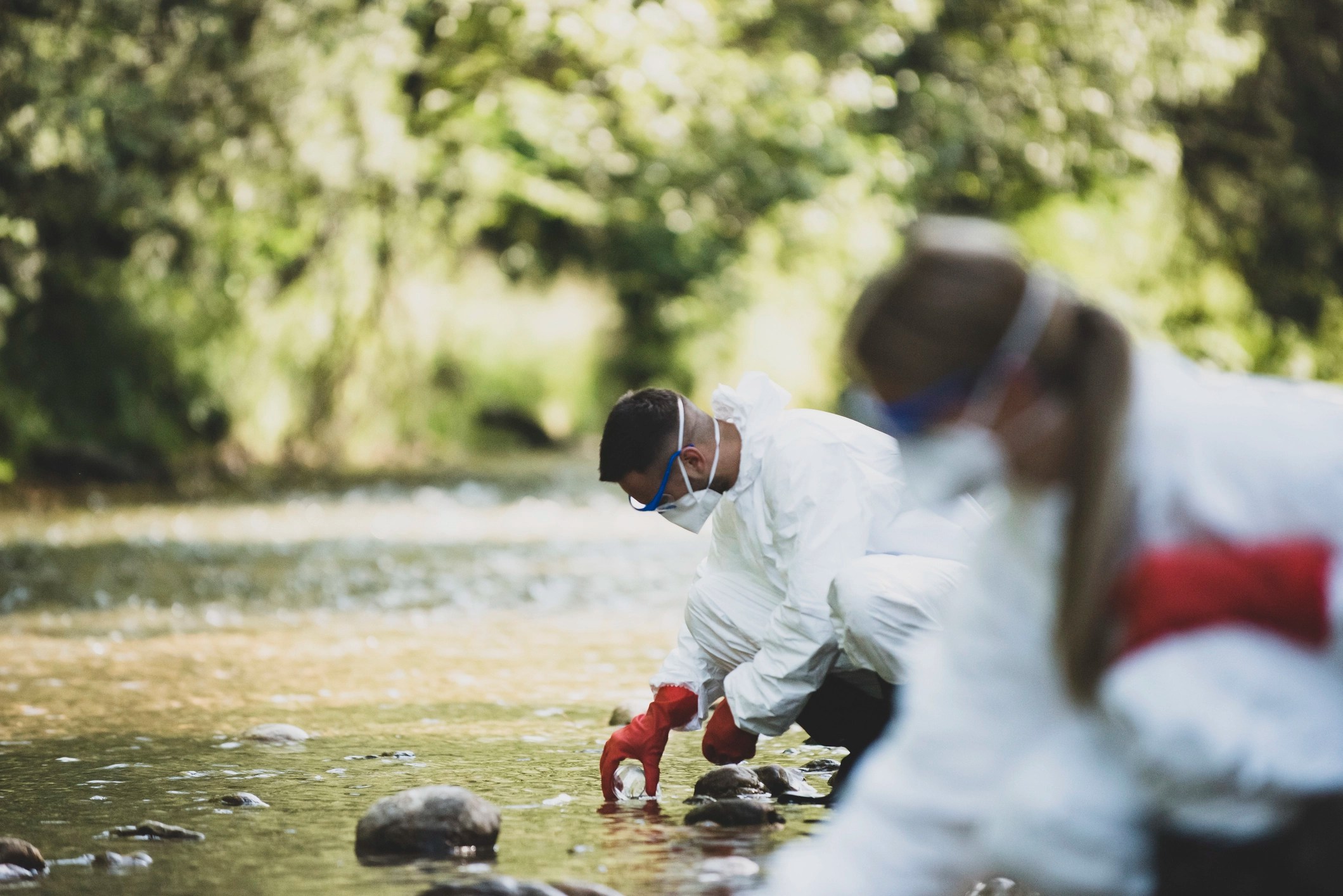 Environmental health professionals in full PPE collecting samples at river.