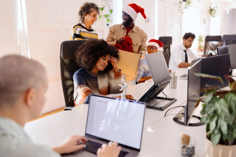 Office worker stressed with holiday-related workload, representing work stress during the busy holiday season and the need for workplace mental health management using ISO 45001:2018 and ISO 45003:2021.