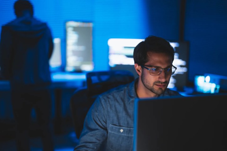 Close-up of a cybersecurity professional analyzing data on a computer screen in a dimly lit office, emphasizing cybersecurity standards.