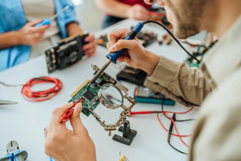 Technician using an ESD-safe soldering iron to work on a circuit board, demonstrating proper ANSI/ESD S13.1-2019 compliant electrostatic discharge protection practices.