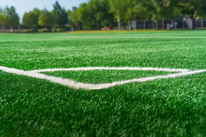 Artificial turf soccer field, adhering to ASTM F1015-03(2017) test methods, with synthetic grass fibers and infill designed for durability, performance, and reduced abrasiveness to enhance player safety during play.