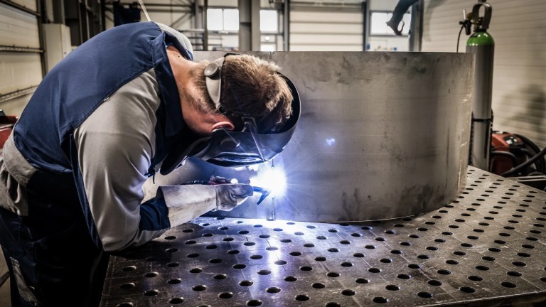 A welder performing a weld on sheet steel, following the guidelines of AWS D1.3/D1.3M:2025 Structural Welding Code for accurate and safe metal fabrication.
