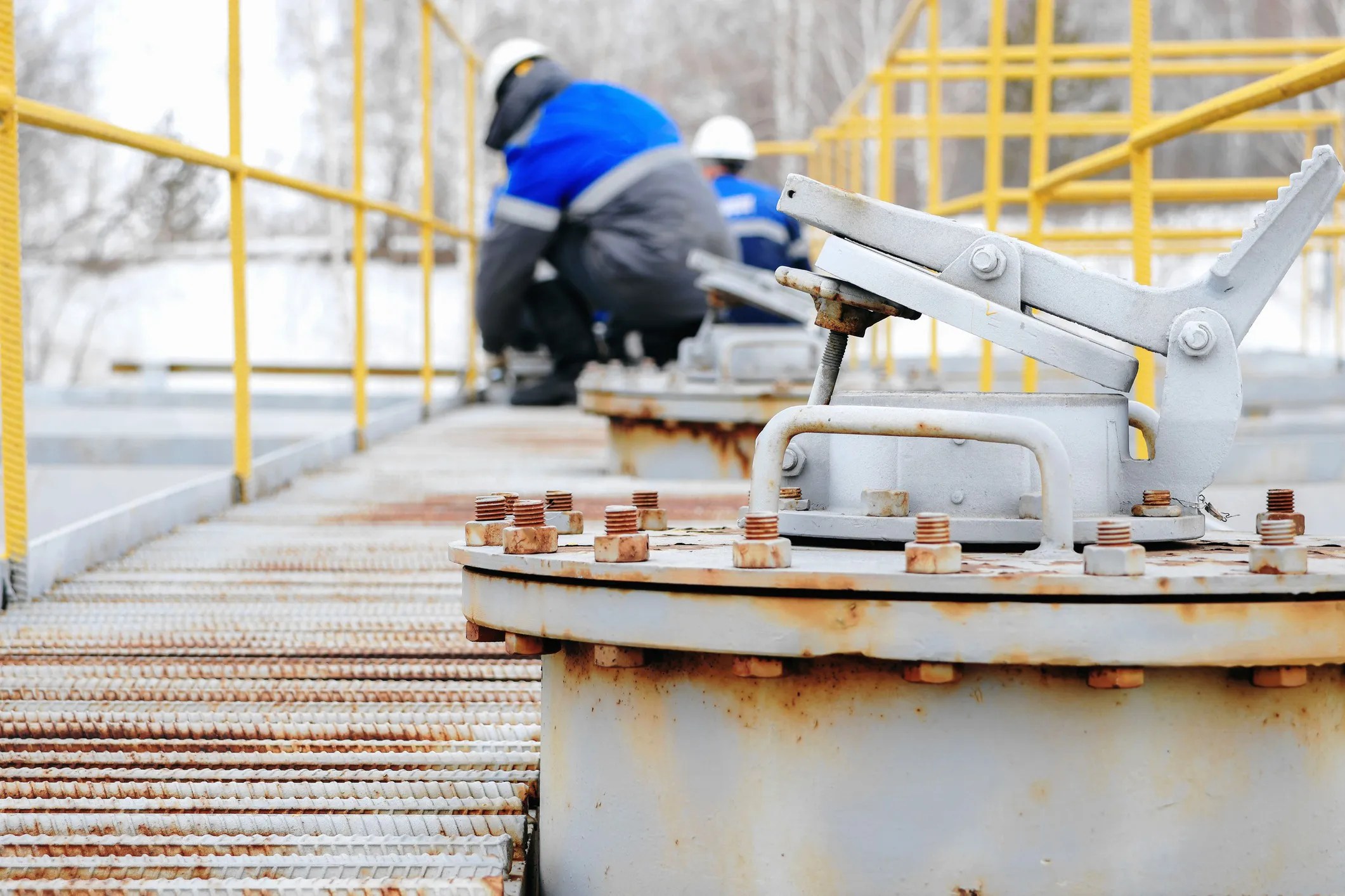 Industrial workers inspecting equipment for corrosion during winter, assessing damage from cold weather and road salt exposure.