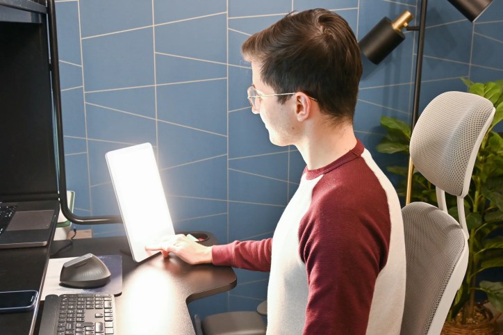 A man working in an office using a sun lamp, adhering to IEC 60601-2-83 Ed. 1.0 b:2019, used for bright light therapy to treat Seasonal Affective Disorder (SAD), improving mood and circadian rhythm during winter months.