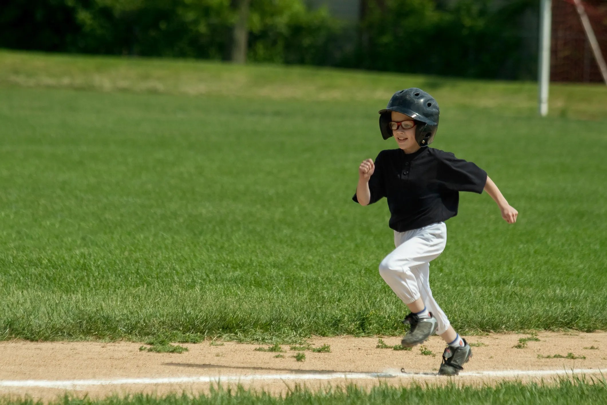 Young boy wearing ASTM F803-25 eye protectors for his baseball game as he runs to first base to prevent any eye injuries.
