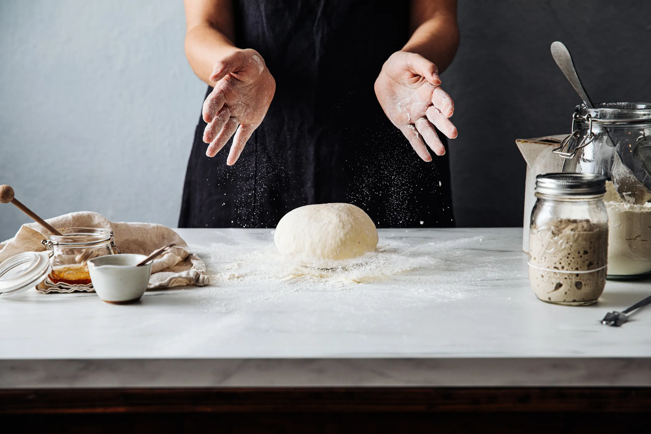 Woman preparing sourdough bread (in accordance to ISO bread-making standards) in the kitchen, with flour, water, and starter visible, showcasing the artisanal baking process.
