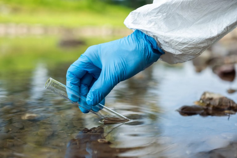Scientist collecting water samples from a river for Clean Water Act 401 compliance testing in an ANAB-accredited laboratory.