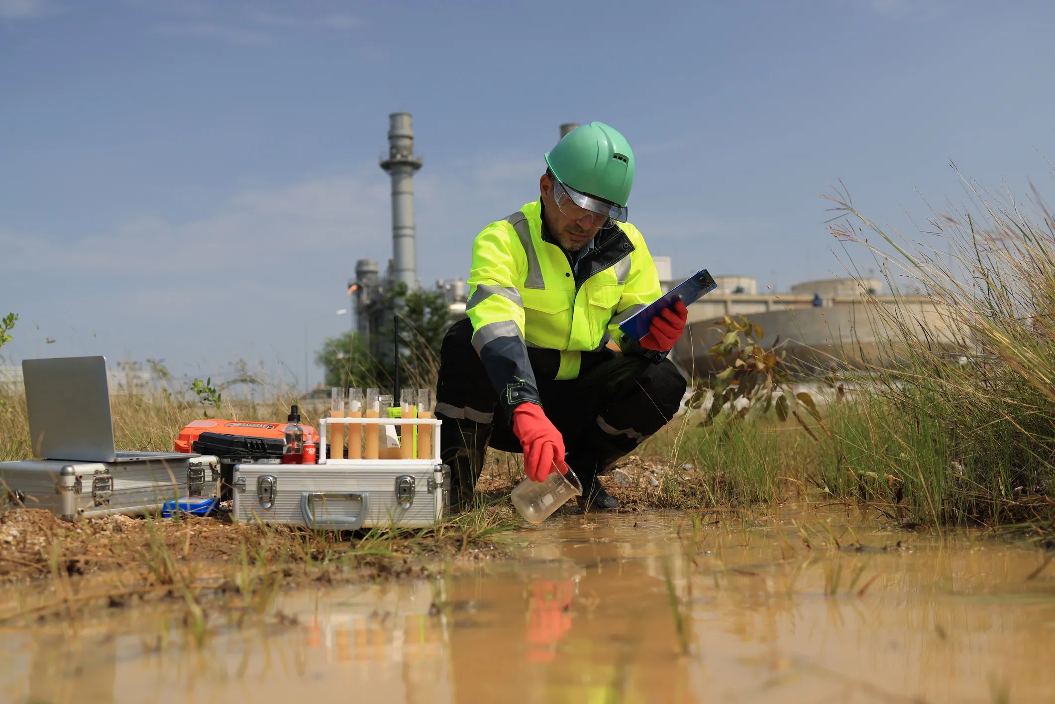 Environmental engineer wearing green safety gear collecting and testing water samples for water quality monitoring and compliance.