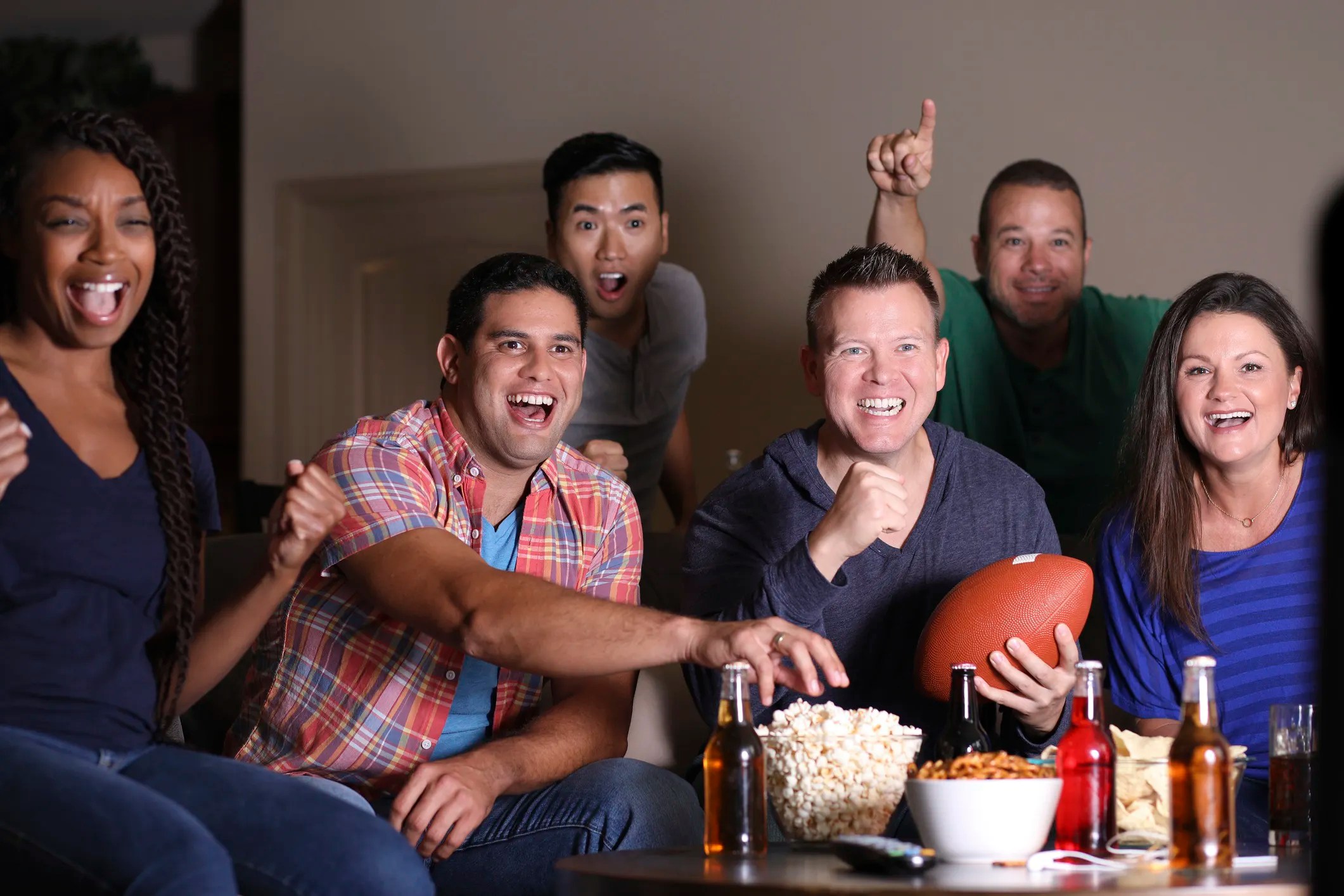 Friends watching the Super Bowl with snacks like popcorn, chips, and beer, enjoying the game thanks to food safety and quality  ISO standards.