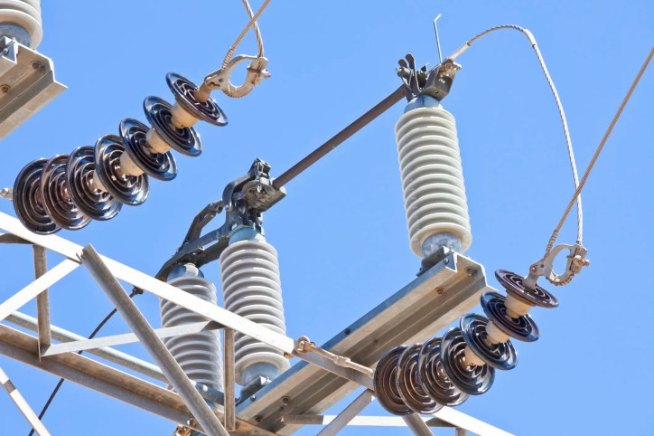High-voltage electrical power insulators on a transmission tower supporting overhead power lines against the sky, adhering to ANSI/NEMA C29.1-2018.