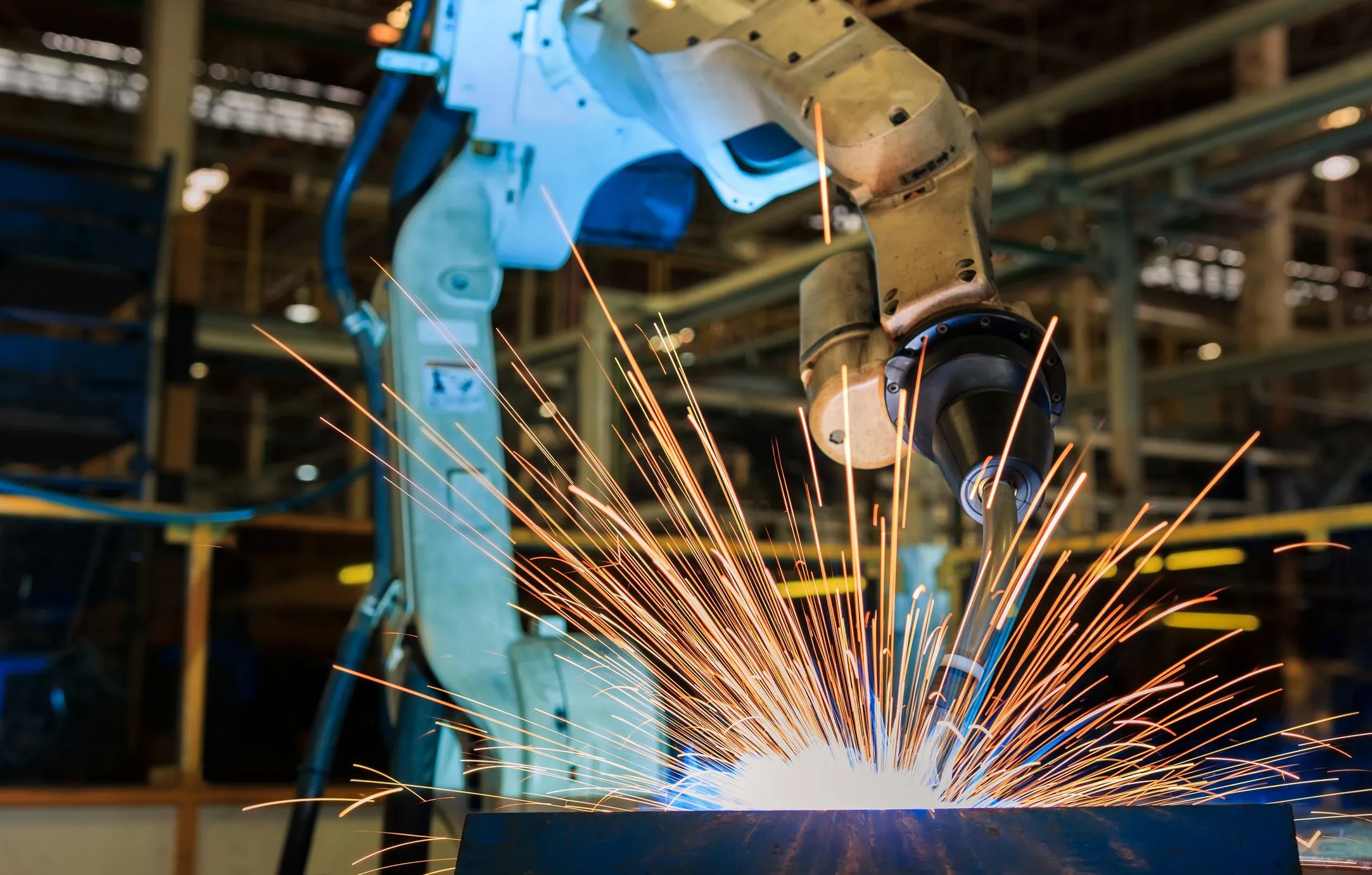 Industrial robotic arm performing automated welding sparks on a steel automotive frame in a modern manufacturing facility.