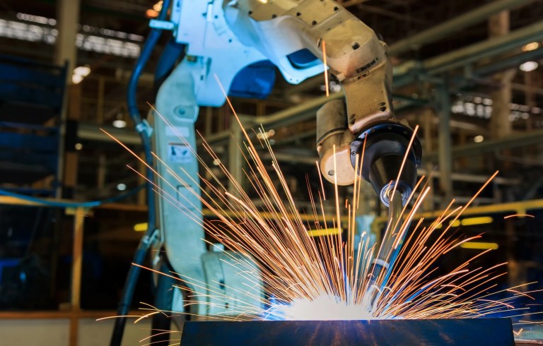 Industrial robotic arm performing automated welding sparks on a steel automotive frame in a modern manufacturing facility.