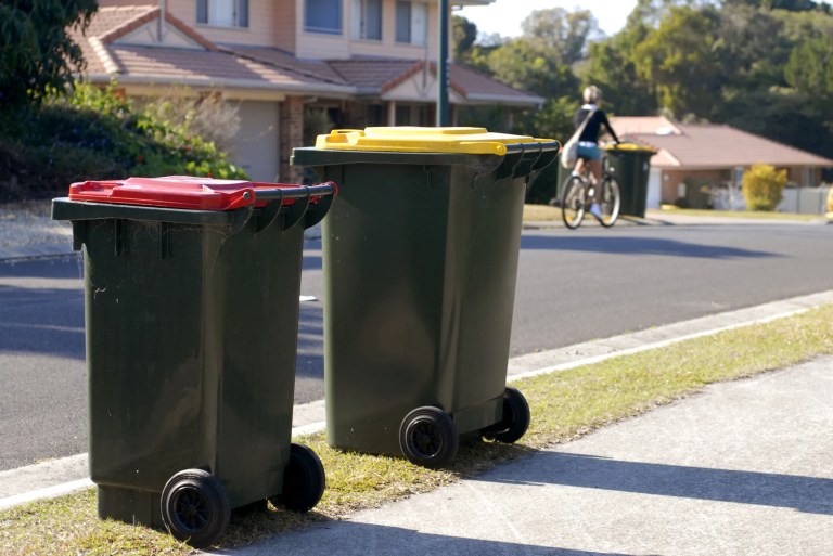 Commercial waste containers outside by the street in compliance with ANSI Z245.30-2018 safety requirements.