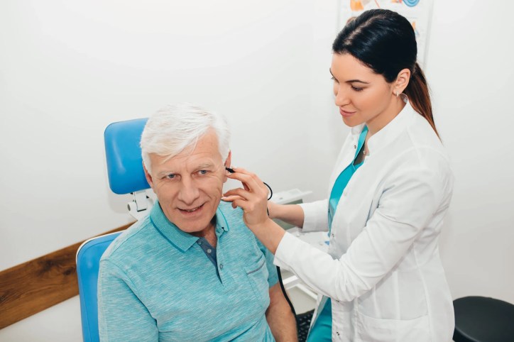 A healthcare professional is fitting an assistive listening system, adhering to ASA/ANSI S3.47-2014 (R2023), for an elderly patient at an audiology clinic, ensuring comfort and proper function.