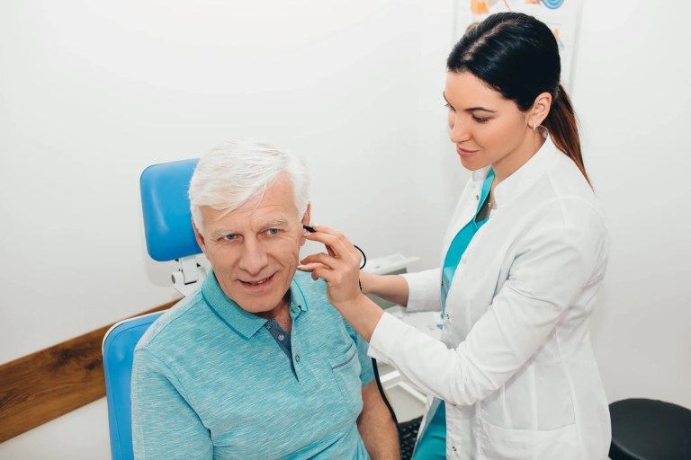 A healthcare professional is fitting an assistive listening system, adhering to ASA/ANSI S3.47-2014 (R2023), for an elderly patient at an audiology clinic, ensuring comfort and proper function.